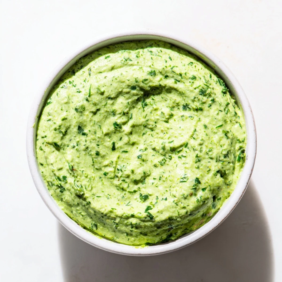 Creamy, vibrant Green Goddess Dip swirled with fresh herbs, ready for dipping vegetables in a bright bowl.