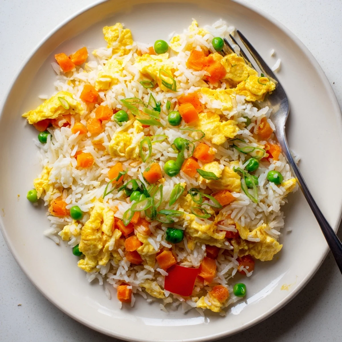 Stir-frying diced bell peppers, peas, and scrambled eggs with savory seasonings to create this quick classic egg fried rice.