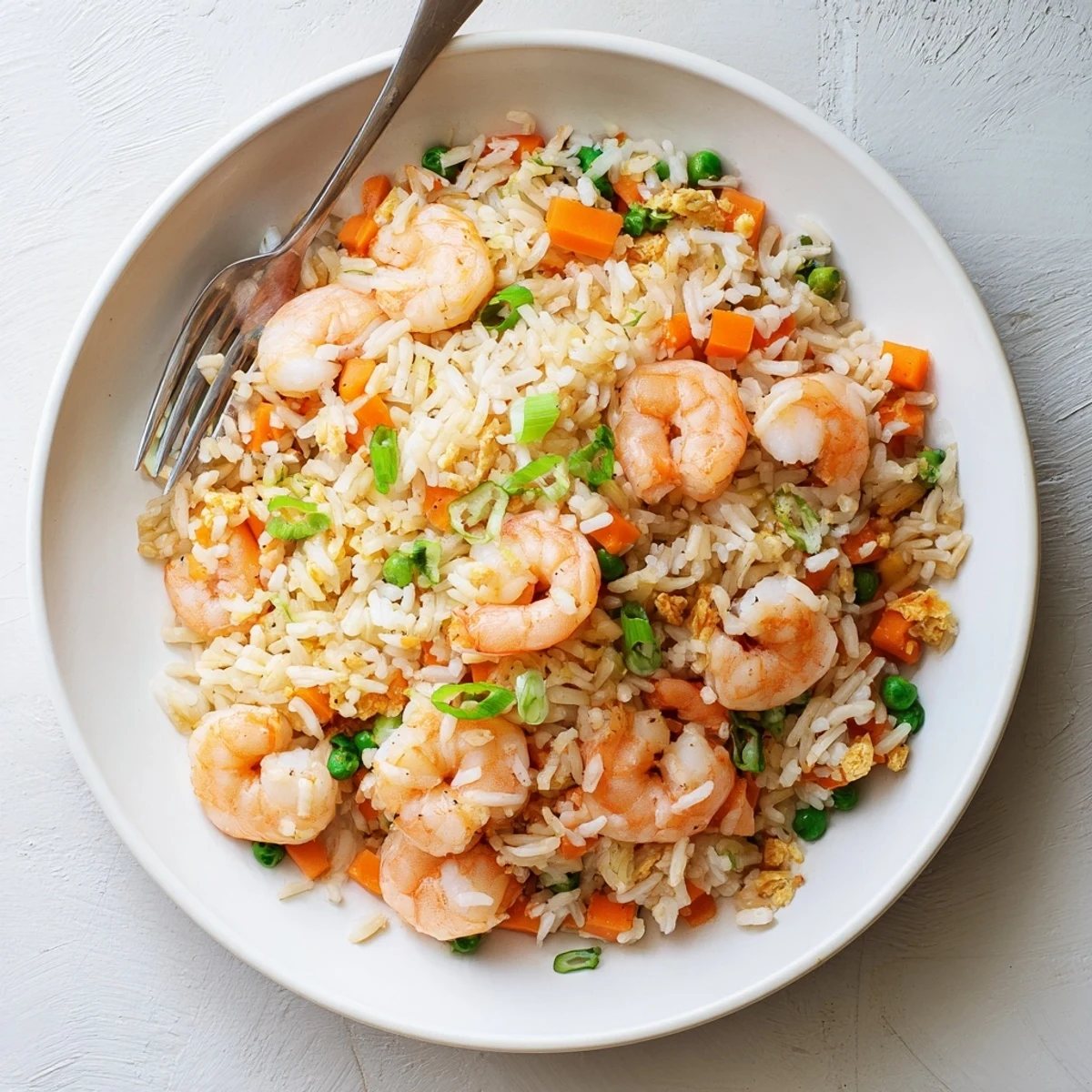 Close-up of Shrimp Garlic Fried Rice piled high in a bowl, garnished with fresh spring onions and lime wedges.