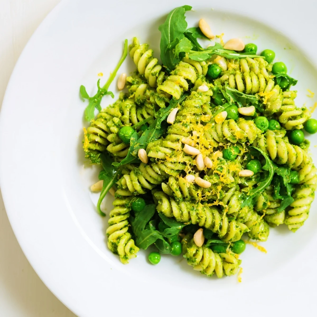 Spring Green Pesto Pasta Salad with peas, arugula, and toasted pine nuts tossed in creamy basil pesto.