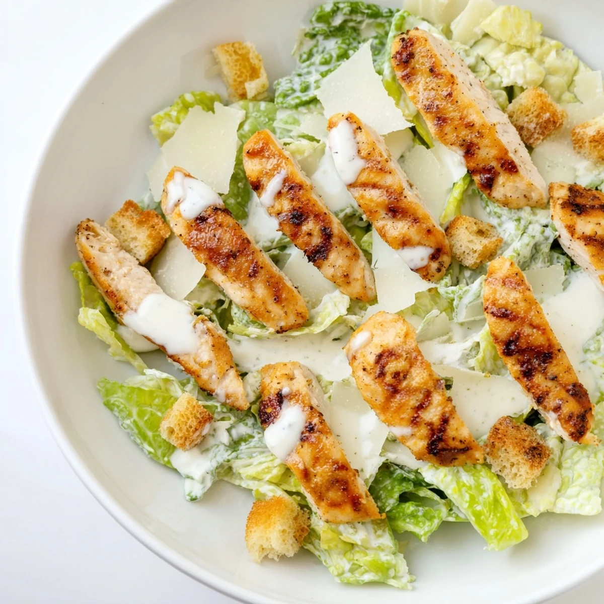 Overhead shot of a hearty Yogurt Caesar Grilled Chicken Salad, showcasing juicy chicken strips, halved cherry tomatoes, and crunchy croutons tossed in creamy dressing.