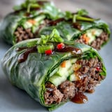 Freshly assembled Thai Basil Beef Rolls sit on a platter, showcasing tender beef, crisp cucumber, and carrots wrapped in translucent rice paper.