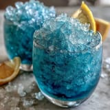 Vibrant blue slushie blending tangy lemon and sweet raspberry, served with fresh mint and lemon slices.