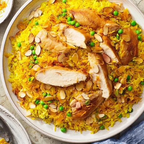 Enjoy a steaming bowl of flavorful saffron chicken and rice pilaf, garnished with toasted almonds and herbs.