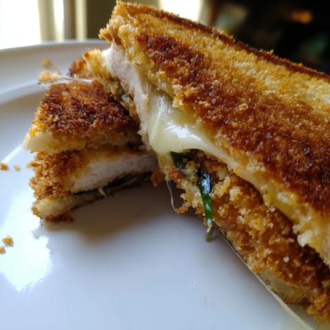 Golden, crispy Parmesan Chicken Thighs Grilled Cheese, oozing melted cheese between toasted sourdough slices, ready to serve.