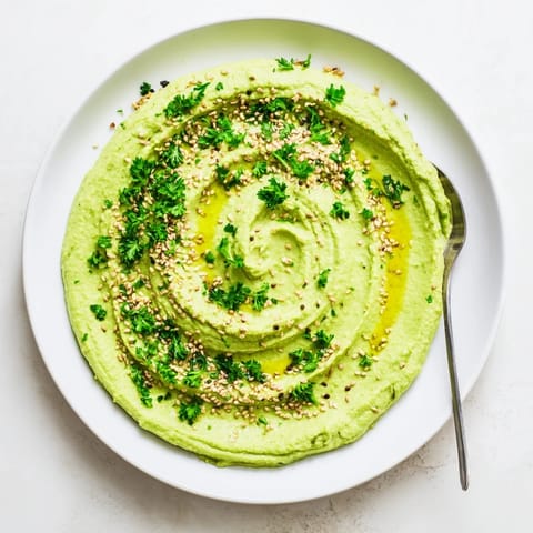 Creamy homemade Edamame Hummus spread on crisp pita chips, alongside colorful raw vegetables like carrots and cucumbers for a healthy snack.