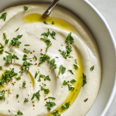 A smooth white bean dip with lemon and garlic, served alongside crunchy pita chips and fresh veggies.