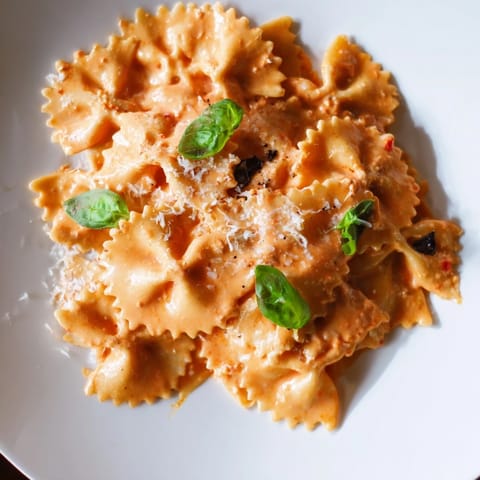 A close-up of Tomato Basil Bowtie Pasta with vibrant red sauce, silky cream swirls, and fragrant basil garnish.  