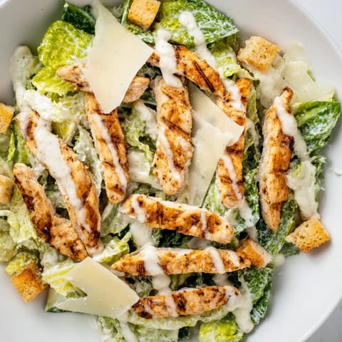 A close-up view of tender grilled chicken breast slices draped over chopped romaine, featuring shaved Parmesan and a light drizzle of tangy yogurt Caesar dressing.