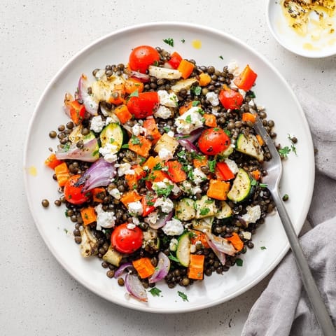 Hearty Black Lentil Salad with Roasted Vegetables served warm in a white bowl, topped with crumbled feta and vibrant cherry tomatoes, ready for lunch.  