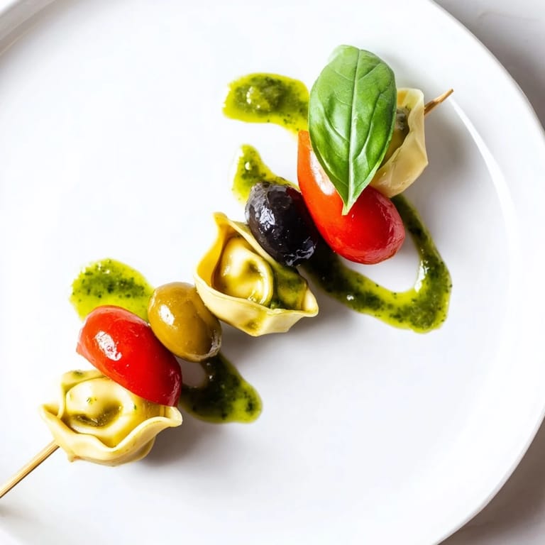 Tender tortellini, tossed in pesto, gleam on appetizer skewers next to bright cherry tomatoes and olives.