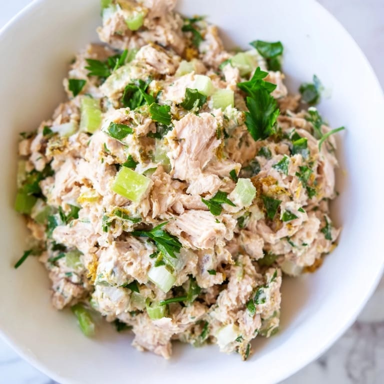 Spicy Zesty Tuna Salad mixed in a bowl with creamy dressing, sliced scallions, and a side of crackers.