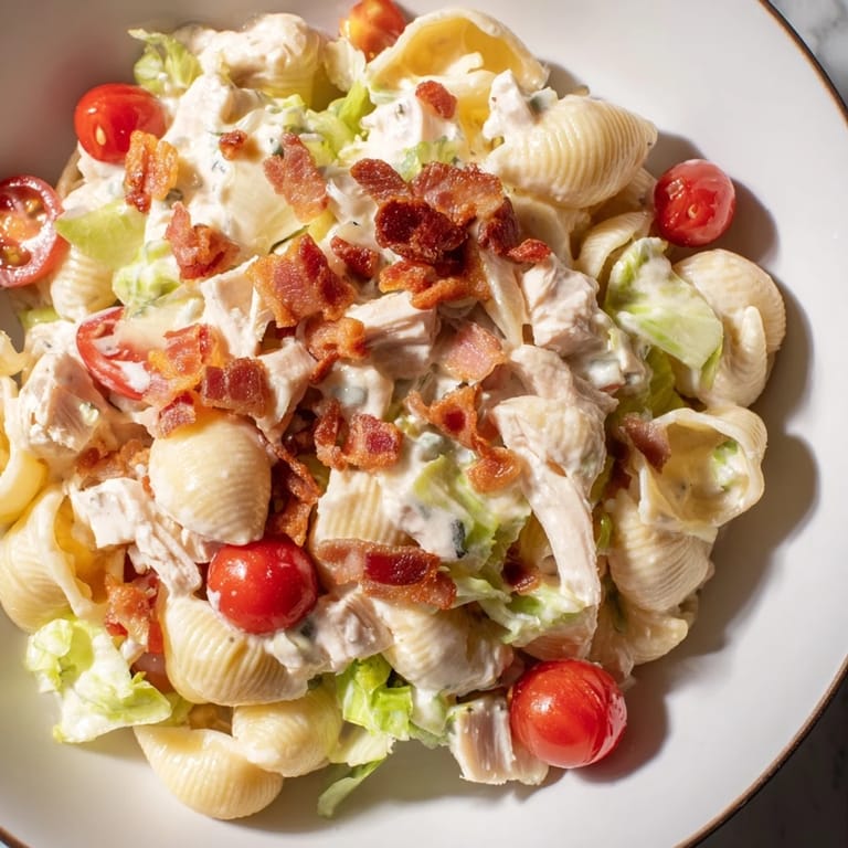 Close-up of creamy BLT Chicken Pasta Salad in a white bowl, featuring tender pasta shells and chopped romaine lettuce.  