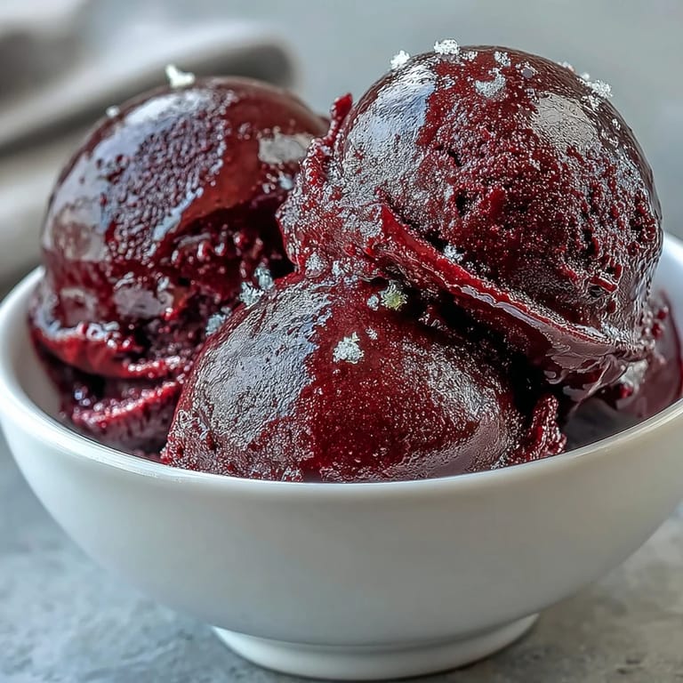 A chilled bowl of Black Currant Sorbet garnished with mint, offering a vibrant vegan dessert served with shortbread.
