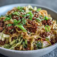 Steaming Potsticker Noodle Bowls with browned pork, crisp cabbage, and carrots are garnished with fresh cilantro and sesame seeds.