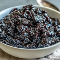 Close-up of glossy Black Currant Reduction sauce drizzled over roasted duck breast on a white plate.